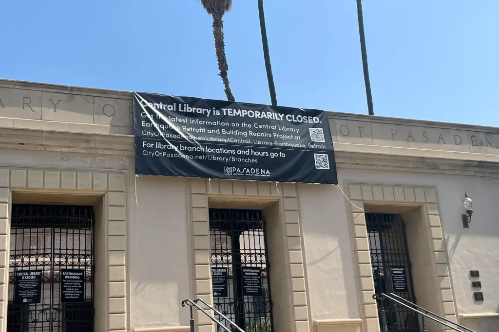 A banner on the Pasadena Central Library announcing that the library is temporarily closed, with web addresses and QR codes for updates and branch hours.